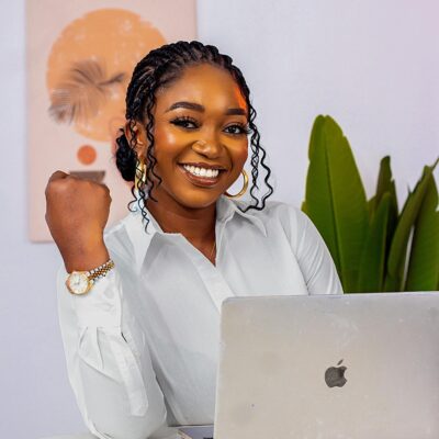 Smiling businesswoman works confidently on a laptop in a creative office setting, embodying modern entrepreneurship.