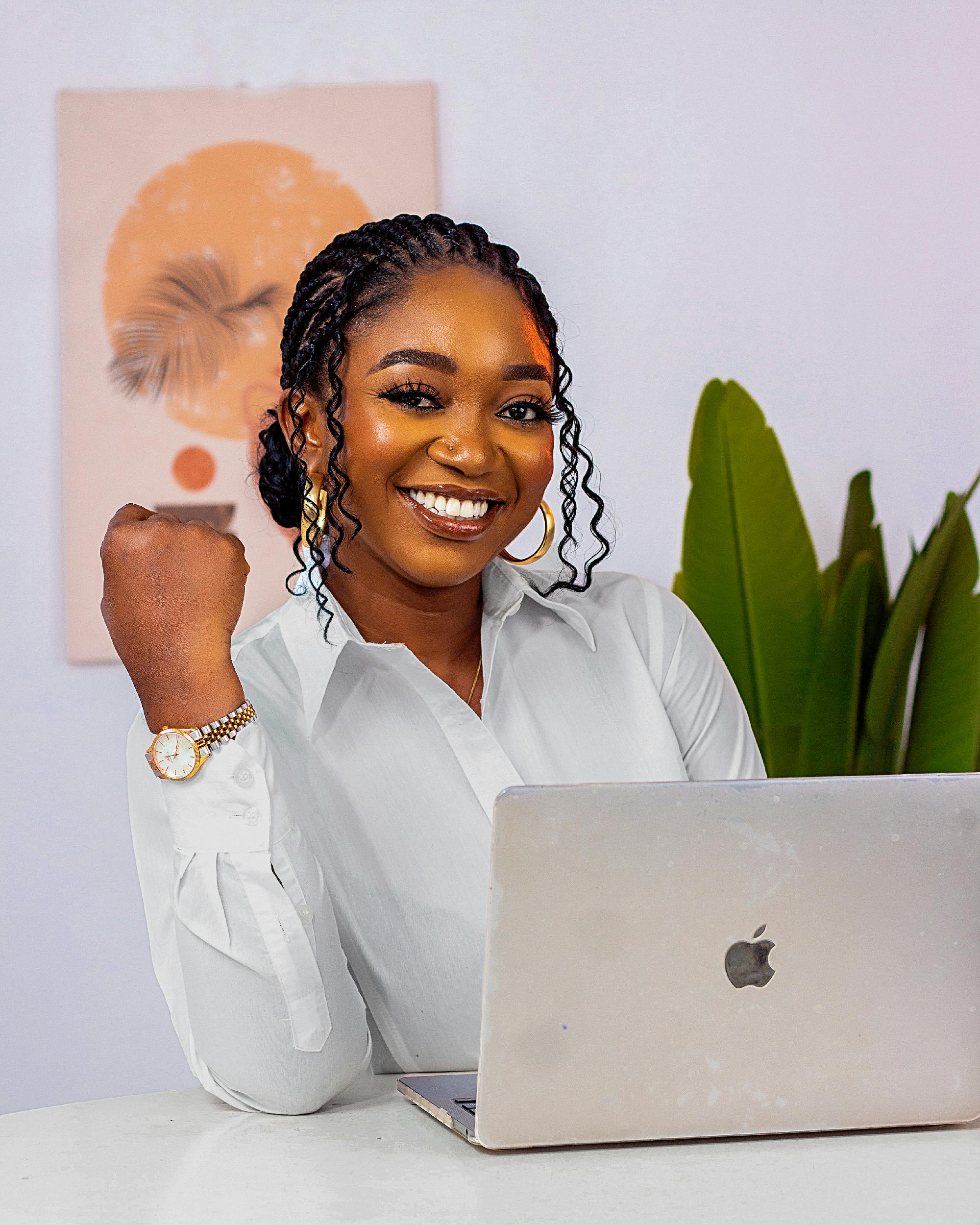 Smiling businesswoman works confidently on a laptop in a creative office setting, embodying modern entrepreneurship.