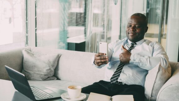 Confident businessman thumbs up during a video call in a relaxed office setting.